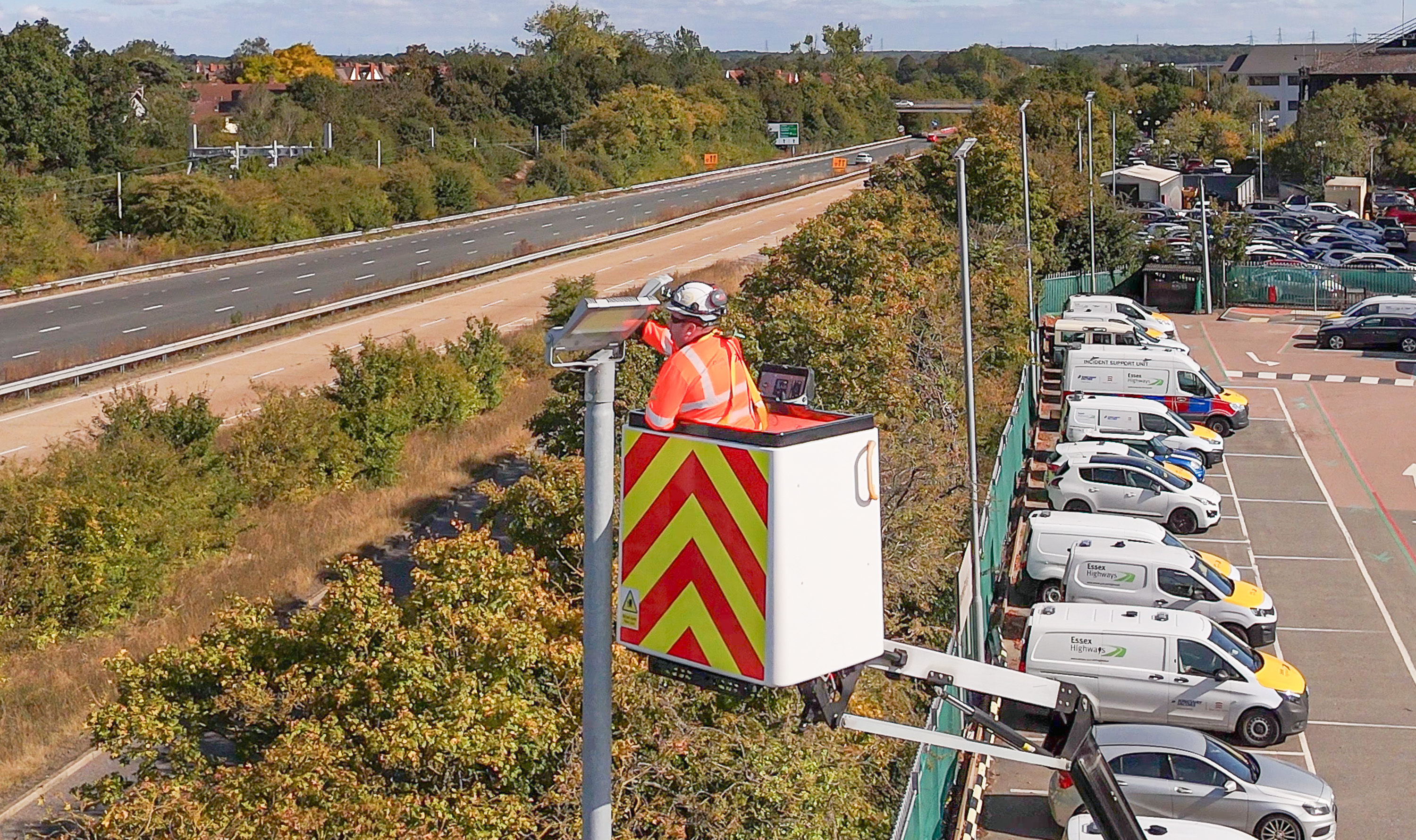 Essex Highways operative working from elevated access platform inspecting lighting infrastructure along dual carriageway and Ringway Jacobs offices.
