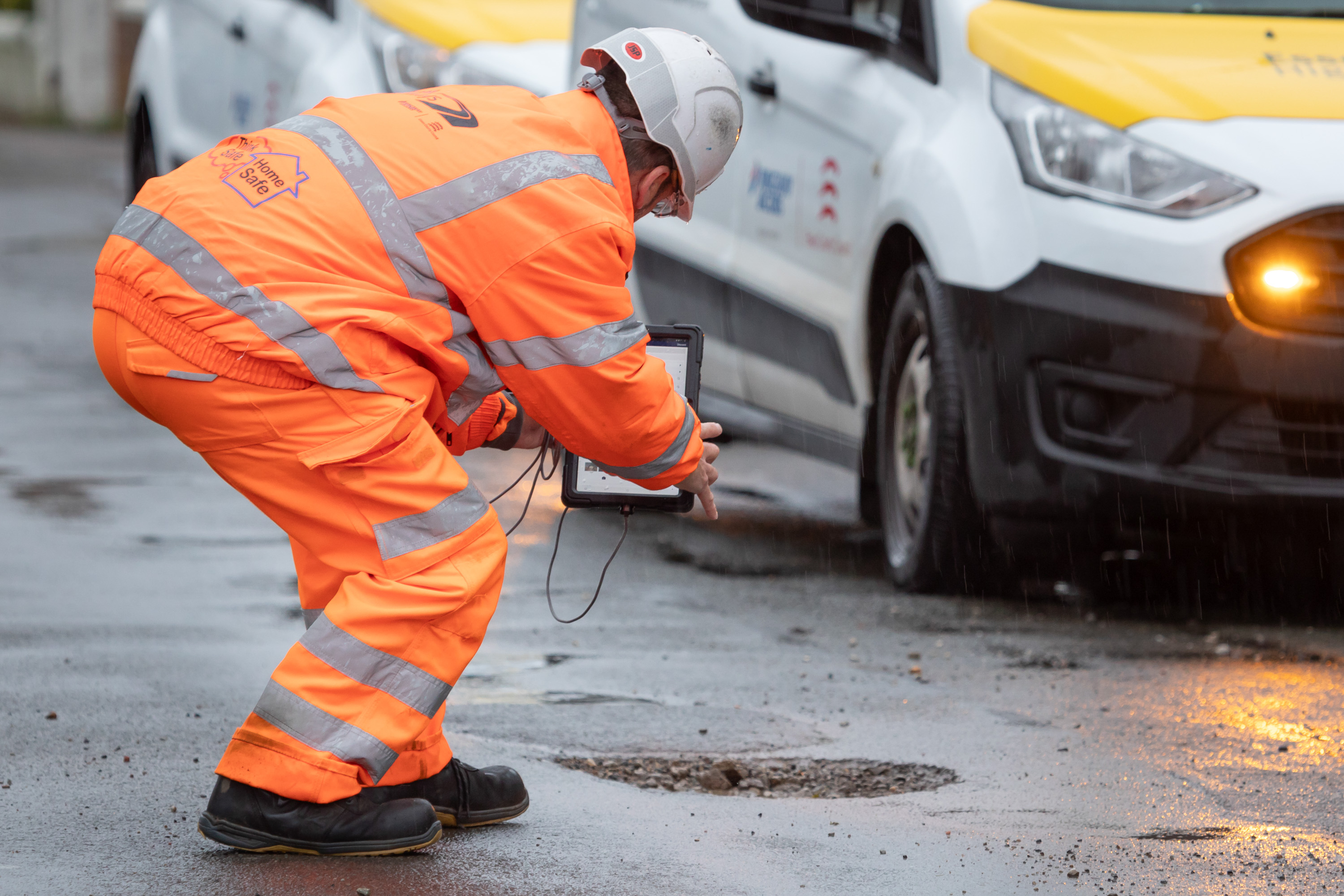 Ringway Jacobs Highways operative photographing a pothole beside service vehicle to record road condition for asset management team